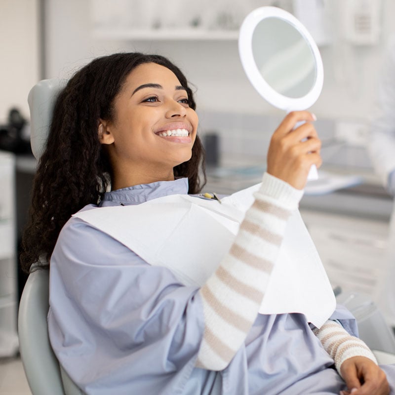 lady smiling in dental chair holding a mirror